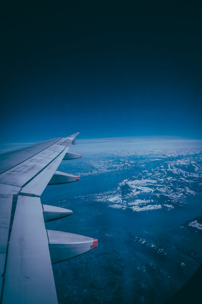 Stunning view of the airplane wing flying over scenic landscapes with snowy mountains below.